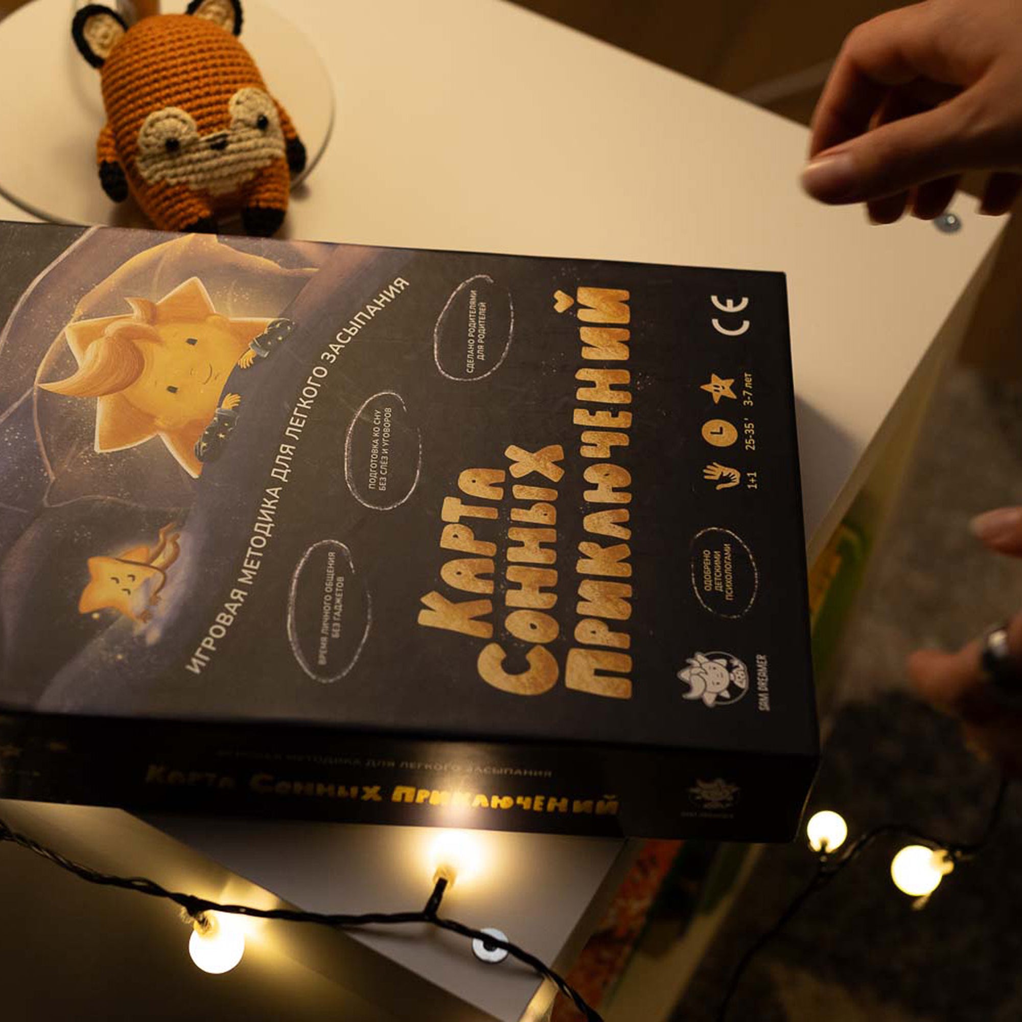 Коробка настольной игры "Карта сонных приключений" на тумбочке с гирляндой