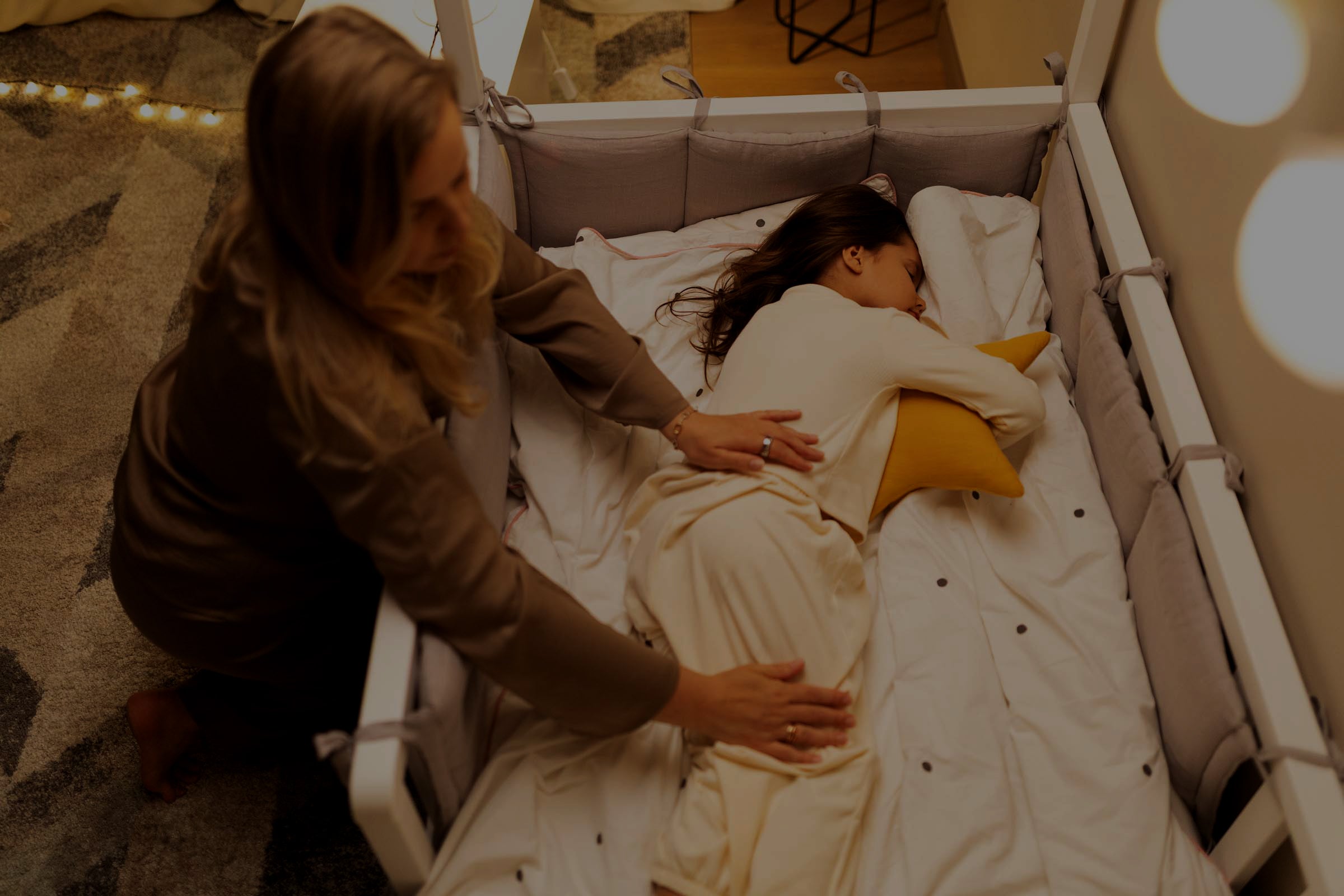“Miega piedzīvojumu karte” fotosesija, mamma guldina guļošo meitu mājīgā bērnu istabā.